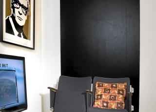 KUNSTVERK: Michael Caine, som henger p� veggen til venstre, er et kunstverk av Conrad Leach. Bak kinostolene mine har jeg hengt opp en svartmalt mdf-plate. Jeg har alltid �nsket meg en svart vegg, men i denne lille leiligheten ville nok en hel vegg blitt litt mye. TV-bordet har jeg lagd av paller som jeg har sagd i to, malt hvite og satt hjul p�. FOTO: Siri M�ller