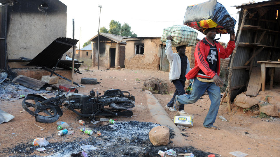 D�DELIGE ANGREP: Natt til s�ndag ble minst 200 mennesker drept i et voldsomt machete-angrep i det sentrale Nigeria. Dette bildet ble tatt i slutten av januar i �r. To nigerianere b�rer sine eiendeler forbi en brent bygning etter et voldelig angrep i Kuru Karama, 30 kilometer fra Jos hvor det nye angrepet fant sted. FOTO: AFP / PIUS UTOMI EKPEI