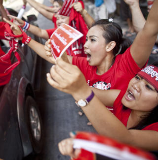 ST�TTER R�DSKJORTENE: To kvinner st�tter deomonstrantene som kj�rer forbi i Bangkok. Prosesjonen ble h�ylydt feiret fra fortauene av mengder av folk som veivet r�de b�nd. Foto: SCANPIX