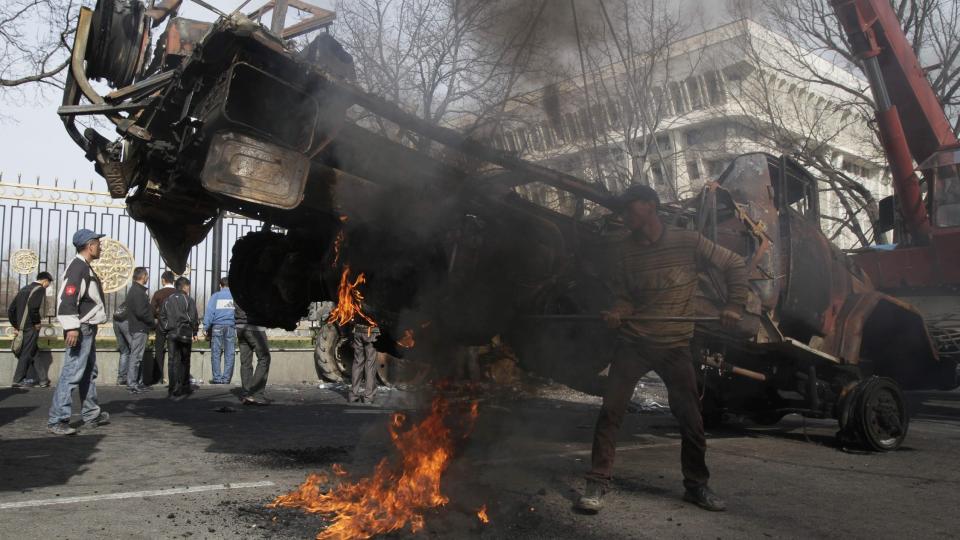 A worker tackles a burning tire from a burnt-out truck before removing it from the square in front of a looted government building in capital Bishkek, Kyrgyzstan, Friday, April 9, 2010. After a night of gunfire throughout Kyrgyzstan's capital, thousands of grieving and defiant residents gathered Friday in Bishkek's main square to mourn victims of this week's revolt that left at least 75 people dead and forced the president to flee. (AP Photo/Ivan Sekretarev)