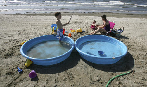 STRANDLIVET FORTSETTER: Bridget Hargrove fra Louisiana har med barna p� stranda tross oljemarerittet. For � kj�le ned varme kropper har de medbragt sv�mmebasseng. Foto: REUTERS/Sean Gardner/SCANPIX