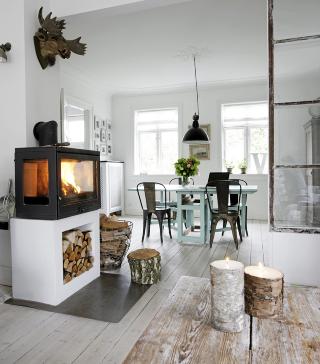 SKAPER VARME: Peisen og glassveggen gir en naturlig oppdeling av stuen. Trelysene i forgrunnen er fra Broste Copenhagen.  FOTO: Linnea Press