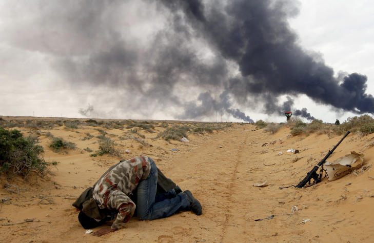 REVOLUSJON: Oppr�rerne kjemper en innbitt kamp mot Muammar Kadhafis sikkerhetsstyrker. Her ber en av dem i veien mellom Ras Lanuf og Bin Jawad med r�yk stigende fra oljeledninger bombet av Kadhafi. Foto: 
  Reuters/Goran Tomasevic/Scanpix