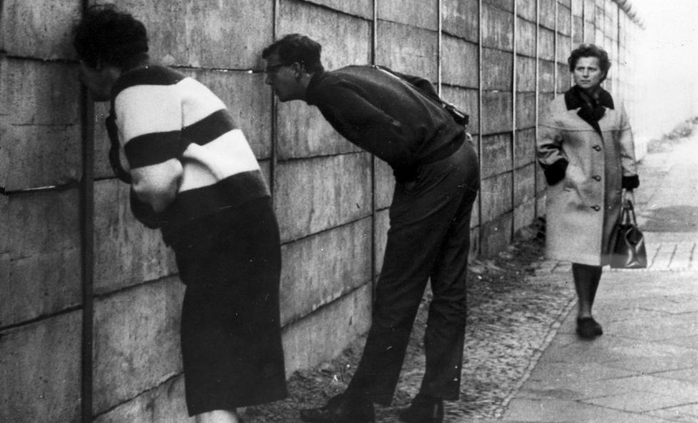 SKILTE TYSKLAND: Det historiske bildet fra Vest-Berlin. I Lindenstrasse i n�rheten av Check Point Charlie, viser at Berlin-muren er nesten ferdig. Muren er p� dette tidspunktet tre meter h�y og er avrundet p� toppen, s� det er vanskelig � f� tak hvis noen skulle �nske � klatre over. Vestberlinere kikker inn i �st-Berlin gjennom sprekker i muren.
Foto: Keystone / Billedsentralen
