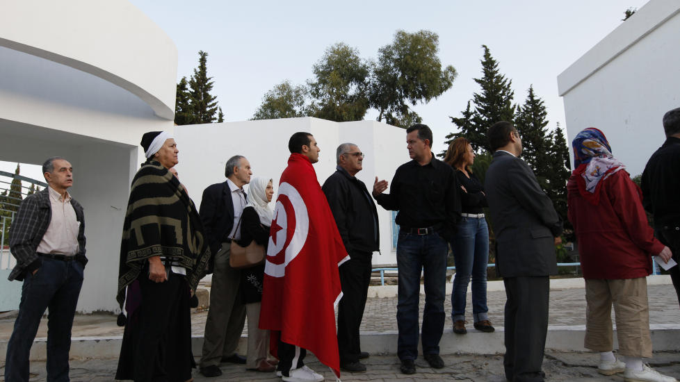K�: En mann har drapert seg selv i det tunisiske flagget mens han venter i k� for � stemme i det f�rste demokratikse valget i Tunisia s�ndag. Foto: REUTERS / Jamal Said