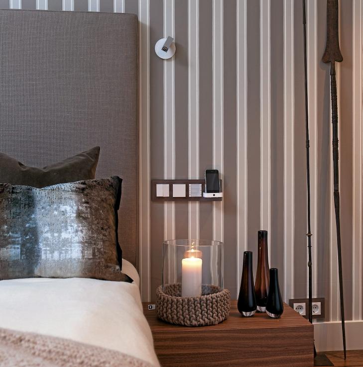 SMART ORDNING: Tapetet bak sengegavlen har striper i samme farge som veggen. Bryterne og mobilladeren ved siden av sengen har passe h�yde over nattbordet. Bryterne Gira Espirit fra Mico Matic har dekorative glassrammer. FOTO: Espen Gr�nli