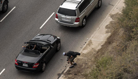 BITER: En fotograf plukker opp bitene av Lohans �delagte bil langs Pacific Coast Highway i g�r. Foto: Scanpix