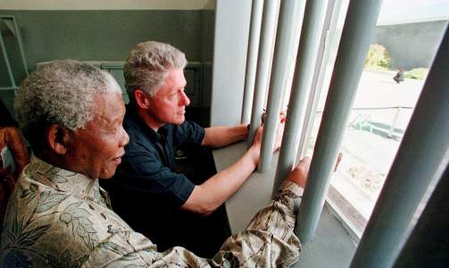 TILBAKE TIL START: Nelson Mandela og den tidligere amerikanske presidenten Bill Clinton kikker ut mellom gitteret som stod mellom Mandela og friheten i 18 av de totalt 27 �rene han satt fengslet. M�tet p� cella p� Robben Island fant sted i 1998, men de to statsmennene har m�tt hverandre flere ganger, b�de f�r og etter. Bill Clinton har blant annet engasjert seg i Nelson Mandela Foundation. Foto: SCANPIX / SCOTT APPLEWHITE