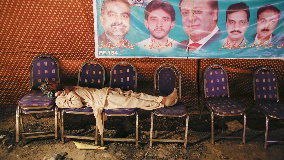 VALGKAMP: En mann tar en cowboystrekk under en plakat med kandidatene fra Pakistans Muslimske Liga. Foto: REUTERS / Damir Sagolj / NTB scanpix