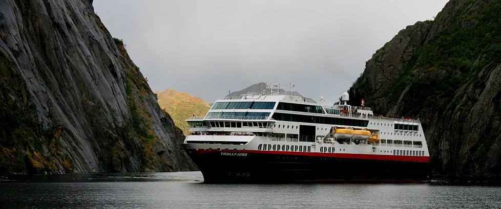 Fjorden ligger rolig med dypbl�tt vann, fossefall og gr�nne bredder