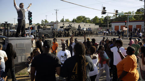 SINTE: En mann forsøker å roe ned en gruppe demonstranter mens politiet i Ferguson står oppstilt i bakgrunnen. Foto: AP Photo/Jeff Roberson SINTE: En mann forsøker å roe ned en gruppe demonstranter mens politiet i Ferguson står oppstilt i bakgrunnen. Foto: AP Photo/Jeff Roberson