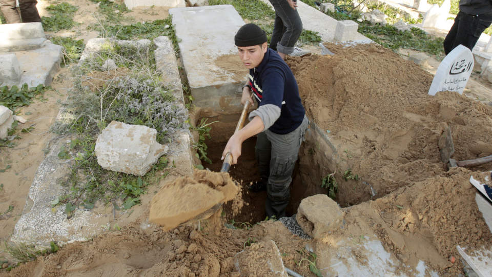 GRAVLEGGER FETTEREN: En palestinsk mann graver en grav til fetteren sin p� Sheikh Redwan-gravstedet i Gaza by. Gravstedet har f�lgende skilt ved inngangen: Gravstedet er fullt. Foto: REUTERS/Mohammed Salem/SCANPIX