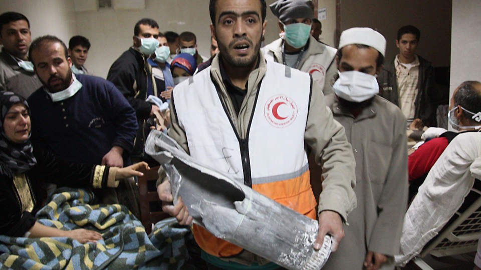 BOMBET SYKEHUS: En ansatt ved sykehuset Al-Quds til R�de Halvm�ne i Gaza st�r igjen med restene av en bombe. Bak ham st�r pasienter med masker som skal beskytte mot alt st�vet i bygningen. Flere hundre gjemmer seg p� sykehuset i frykt for flere israelske bomber. Foto:AFP/MEHDI FEDOUACH/SCANPIX