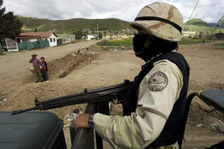 KONTRASTFULLT LOKALMILJ�: Innbyggere i Tijuana-omr�det betrakter de tungt bev�pnede soldatene som bevokter omr�det der Santiago Meza Lopez skulle snakke til pressen. Foto: Guillermo Arias/AP/Scanpix