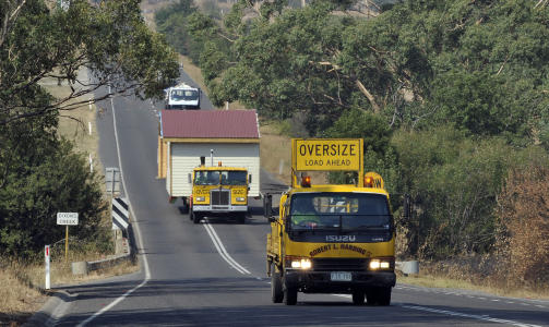 STENGER OG EVAKUERES: En tungtransport med en bygning finner veien ut av brannherjede Yarra Valley. I dag stenges hundrevis av skoler og barnehager i omr�det p� grunn av frykten for at brannene skal blusse opp igjen. Foto: AFP/Paul CROCK/SCANPIX