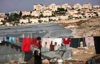 BOR TETT:  En beduin henger opp kl�rna sine like ved den stadig voksende bosetningen Maale Adumim, som ligger like ved Jerusalem - og som er ulovlig hvis du f�lger internasjonale lover og regler. Palestinere og israelske bosettere bor etterhvert tett i tett p� Vestbredden. Forskjellen er at israelske settlere kan bevege seg fritt - mens palestinere m� gjennom utallige sjekkposter og stengte veier. Foto: Menahem Kahana/Afp/Scanpix