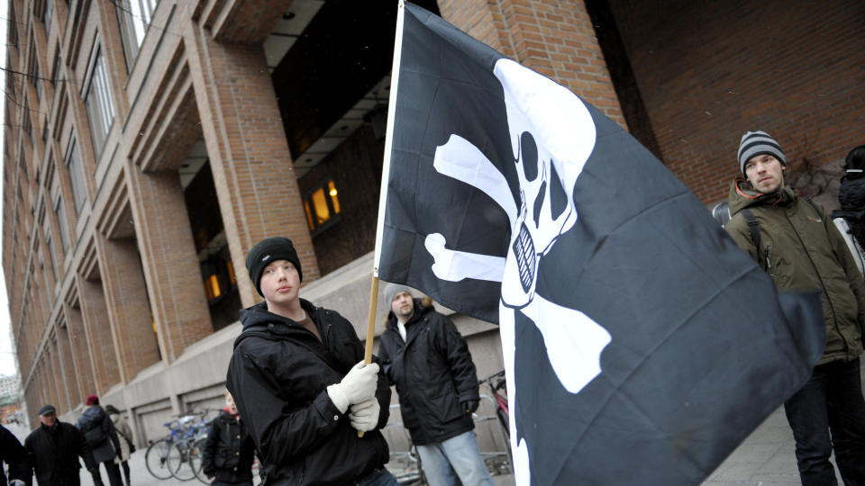 FLAGGET TIL TOPPS, MEN IKKE I RETTSSALEN: Det var The Pirate Bays tilhengere som viste piratflagget under �pningen av rettssaken i Stockholm. Blant de tiltalte var br�kjekkhet og nettvisjoner erstattet av et systematisk fors�k p� � bagatellisere The Pirate Bays betydning for nettsamfunnet, og de tiltaltes betydning for The Pirate Bay, skriver DB.nos kommentator. Foto: SCANPIX