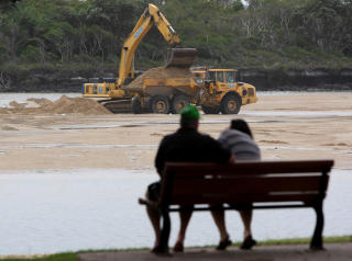 RYDDER OPP: Arbeiderne tok i bruk gravemaskiner for � frakte vekk den forurensede sanden i Coolum, Queensland i g�r. Foto: Scanpix