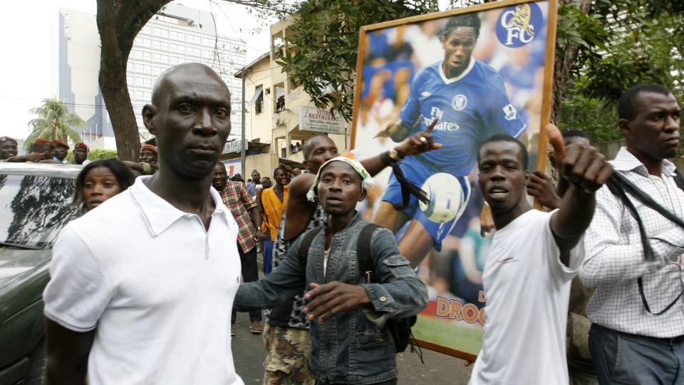 I SORG: Venner og slektninger av de drepte i tribuneulykken gestikulerer foran et portrett av landslagsstjernen Didier Drogba. Ivorianeren sier han fortsatt er p�virket av hendelsen f�r kveldens kamp mellom Liverpool og Chelsea. Foto: SCANPIX/REUTERS/Luc Gnago