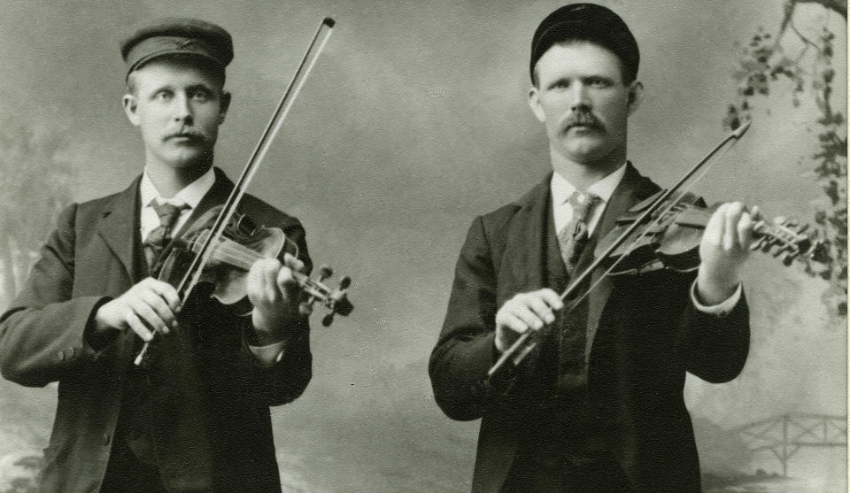 STYGG SOM FAN SJ�LV: �Den amerikanske musikken er stygg som fan sj�lv, (...) dei hev sj�lvsagt h�yrt so lenge paa uljod at dei er utskjemde�, skrev en lite imponert Gunnar Austeg�rd i et brev hjem til Norge i 1928. Andre utvandrede nordmenn fortsatte � spille tradisjonsmusikk �over there�. P� dette bildet fra 1890-tallet st�r den kjente felespilleren Hallvar S. Rysstad sammen med Knut A. Helle foran et naturromantisk bakteppe.Foto: UKJENT