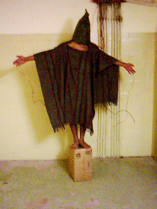FESTET TIL LEDNINGER: En Abu Ghraib-fange blir tvunget stil � balansere p� en boks, med hette over hodet og ledninger knyttet til kroppen. Foto: AP/SCANPIX