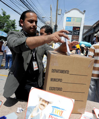 AVGIR STEMME: En mann st�tter den bortf�rte presidenten i Honduras ved � gi en symbolsk stemme for valget som skulle ha v�rt i dag. Presidenten ble hentet i sitt hjem og fl�yet til Costa Rica. Foto: AFP PHOTO Orlando SIERRA.