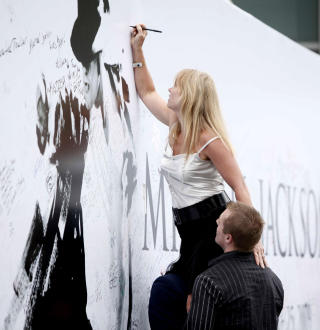 MINNEVEGG: En fan skriver en siste hilsen til Michael Jackson p� minneveggen utenfor Staples Center i Los Angeles i dag tirsdag. Foto: SCANPIX