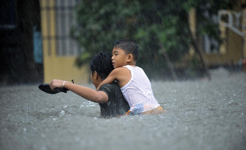 STREVER: En mann b�rer en liten gutt gjennom de oversv�mte gatene i Manlilas forstad Quezon. Foto: JAY DIRECTO/AFP/SCANPIX