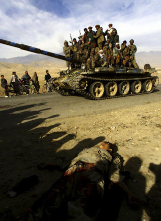 KRIG I AFGHANISTAN: Nordalliansens krigere kj�rer forbi en drept soldat p� vei til Kabul 13. november 2001. De ble tatt godt imot av mange sivile da de inntok hovedstaden. Foto: REUTERS/Yannis Behrakis