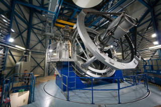 INNI KUPPELEN: VISTA-teleskopet. P� bildet til �verst sees det 3 tonn tunge infrar�de kameraet under monteringsfasen. For � f� en f�lelse av st�rrelsene, legg merke til personen til venstre p� begge bildene. Foto: ESO