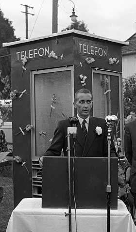 PYNTET TELEFONKIOSK: Leder i Telefons�kendes forening John Gi�ver Gi�ver taler med den vakkert blomsterpyntede telefonkiosken i bakgrunnen. Han hyllet Telefonanlegget, som 86 �r etter at telefonen ble oppfunnet hadde kunnet bringe dette tekniske mesterverk ut til Ekraveiens beboere, om ikke en til hver, s� i alle fall en p� deling.