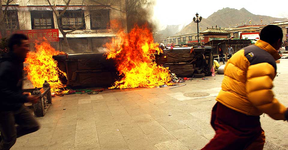 LHASA I BRANN: En munk l�per forbi en brennende bil i Lhasas gater 14.mars.